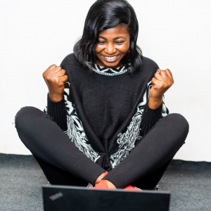 An excited woman sitting on the floor in front of a laptop