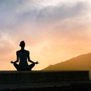 woman outside sitting in yoga position on the group as the sun rises