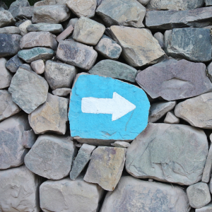 a stone painted blue with a white arrow pointed right in the middle of other stones