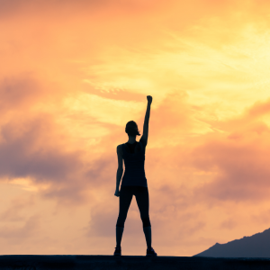 a woman standing on a mountain with one fist in the air as the sun rises