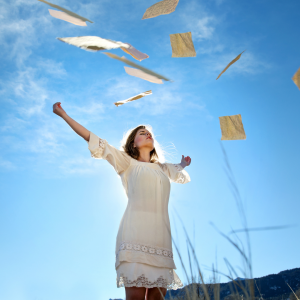 A woman standing in the field throwing papers in the air
