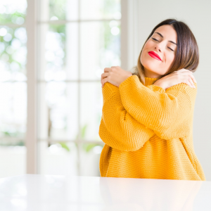 A woman in a yellow sweater happily hugging herself