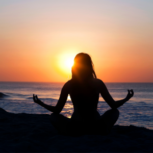 A woman on a beach in a yoga pose while the sun rises