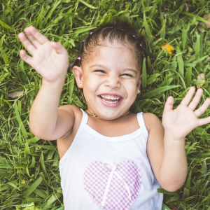 A young girl in the grass looking up to the sky laughing very hard