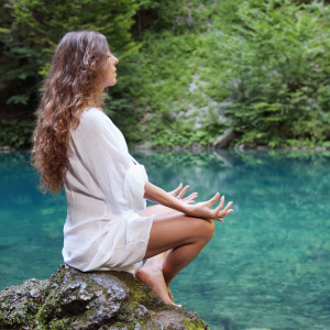 Woman sitting on a rock meditating near a lake
