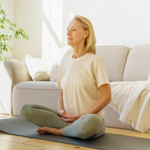 A woman sitting on her yoga mat and in front of her couch with her hands below her stomach breathing deeply