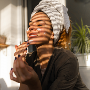 A woman smiling while putting on her facial mask in front of her window