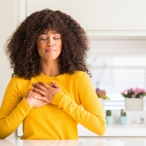 A woman standing in her kitchen with her hand over her heart and her eyes closed
