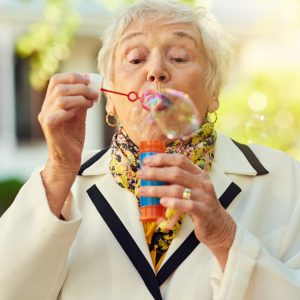 An elderly woman outside having fun while blowing bubbles