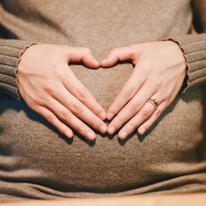 A pregnant woman forming a heart with her hands on her belly