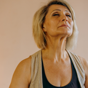 A woman sitting down in an empty room with her eyes closed taking a deep breath