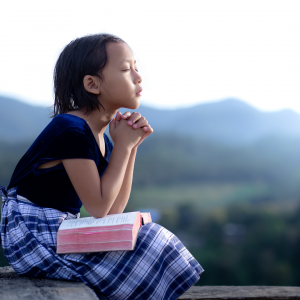 A little girl sitting outside prayer while the sun rises