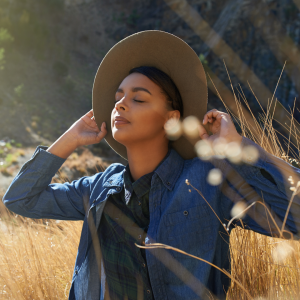 A woman with a sun hat standing in the middle of a wheat field listening to the open field