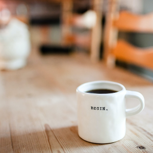 A cup of coffee that saids "Begin" on a wooden table