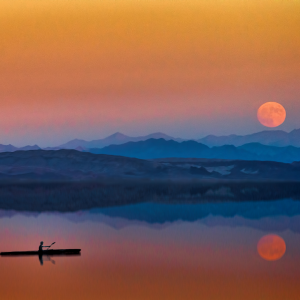 A wide view of a woman in a kayak traveling along a huge lake while the sun rises