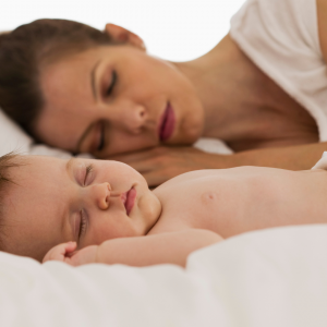 A woman and her newborn baby sleeping together on a bed