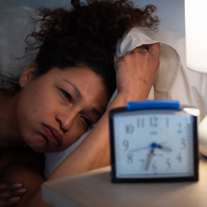 A woman looking at the clock while laying down, not able to go to sleep
