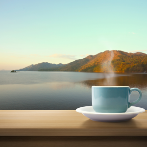 A coffee cup sitting on top of a balcony ledge overlooking a lake
