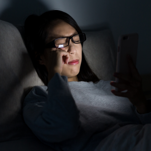 A woman sitting on her bed in the dark looking at her phone crying