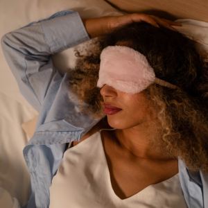 A woman sleeping comfortably in her bed with a fuzzy pink sleeping mask on