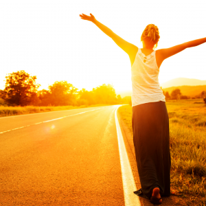 A woman standing in the open road with her arms freely in the air as the sun rises