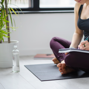 A woman sitting on her yoga mat writing in her journal