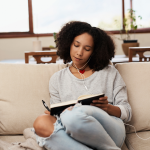 A woman sitting on her couch with her headphones in writing in her journal