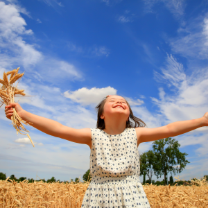 A little girl in a wheat field happily running with her hands in the air