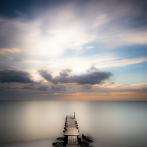 A view of a dock leading to a clear open lake with smooth clouds in the sky