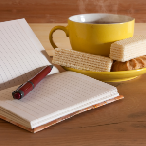 A journal and a plate of wafers and a cup of coffee on a table